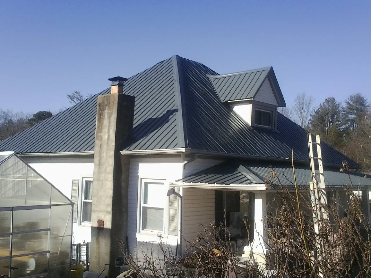 Dark blue standing seam metal roof on a white farmhouse with dormer — Slate & Tile Roof Repair by Roofing Brothers in Smithtown