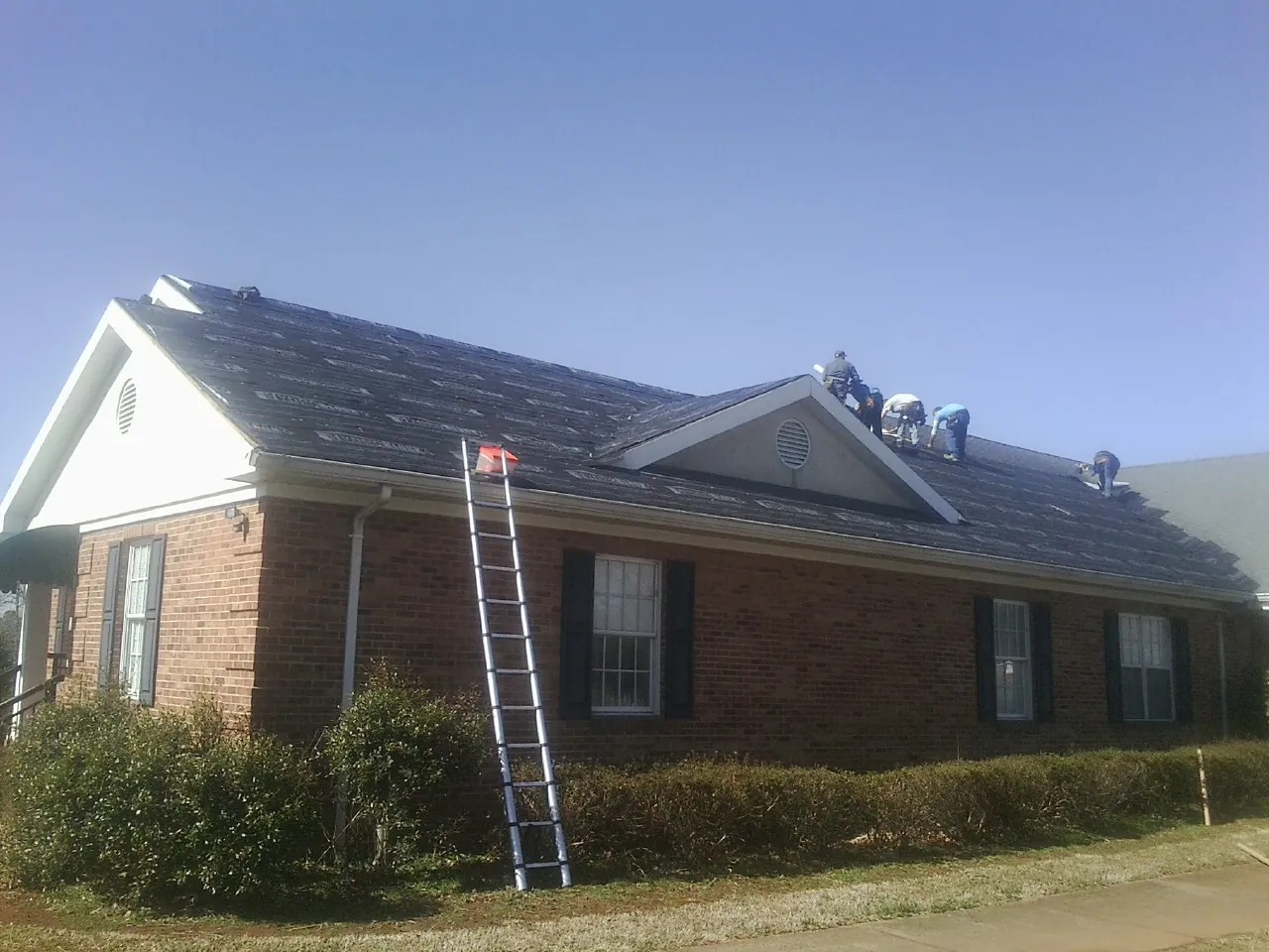 Crew tearing shingles off a brick ranch roof with a ladder set — Emergency Roof Repair work by our crew in Smithtown
