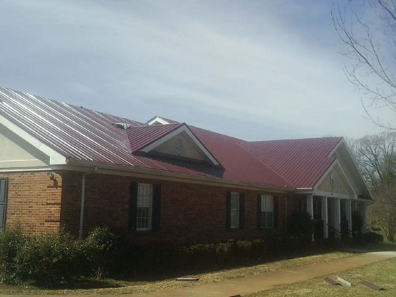 Red metal roof with gabled entries on a long brick building, from a Hail Damage Roof Repair job in Smithtown