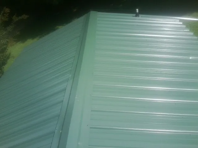 New green metal panels meeting at the ridge of a roof — Flat Roof Repair work by our crew in Smithtown