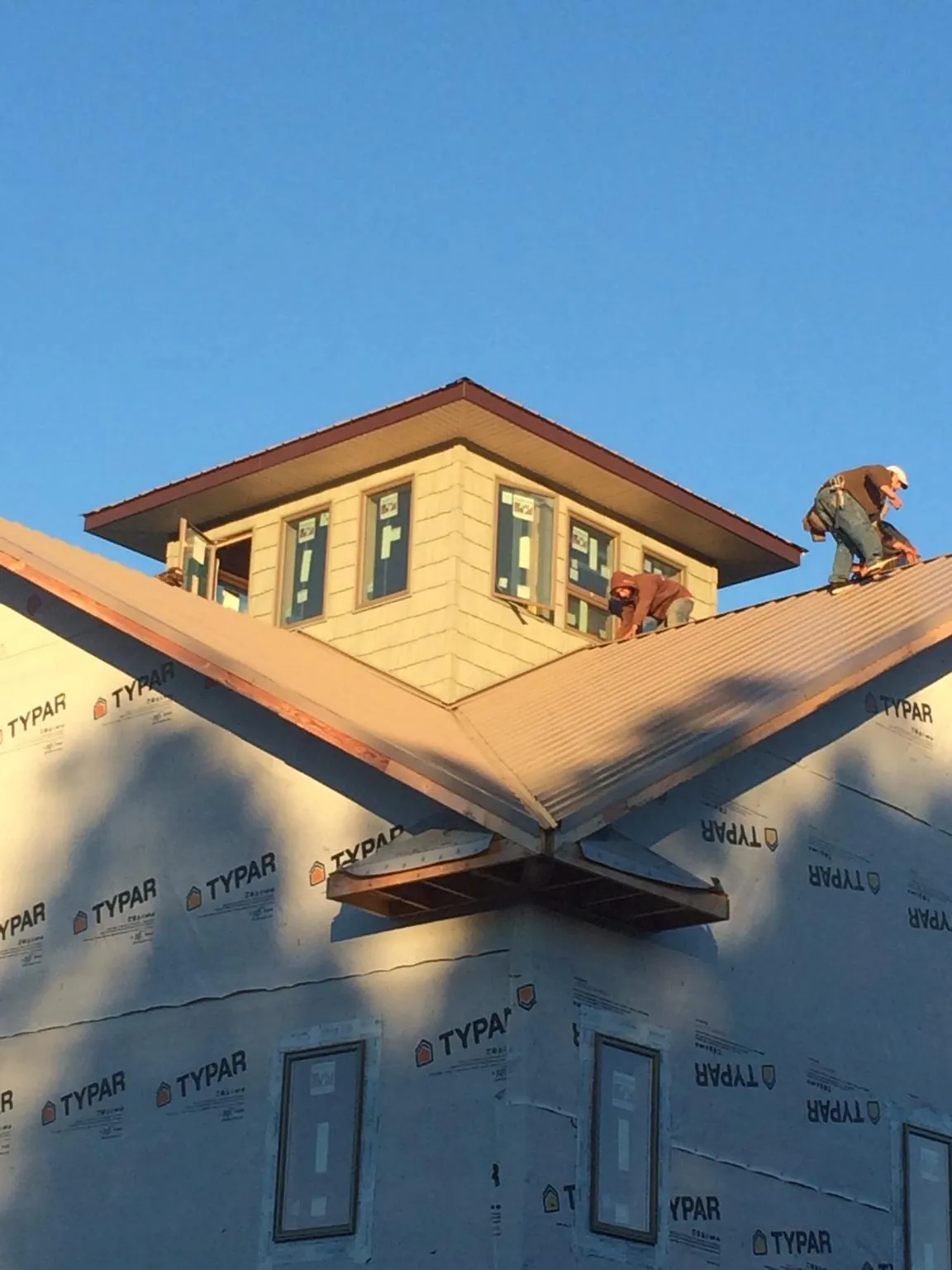 Roofers working around a rooftop cupola on a new metal roof at sunset — Roof Waterproofing in Smithtown by Roofing Brothers